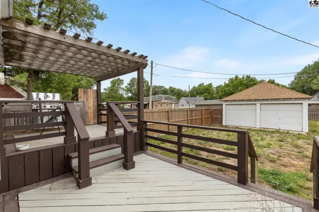 Spacious wooden deck with a pergola and built-in grill overlooks a fenced backyard with a detached garage.