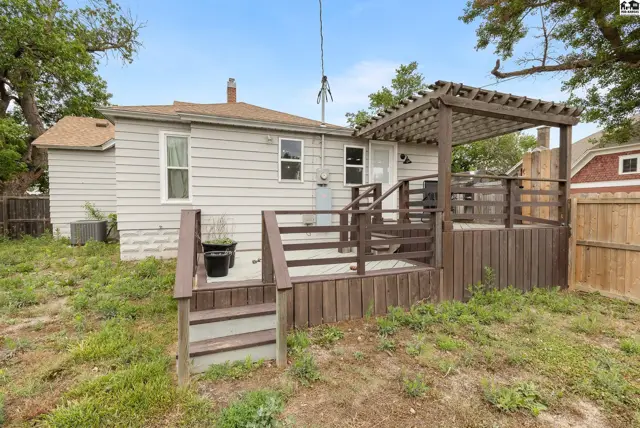 Spacious wooden deck with pergola and stairs extends from the rear of a light-colored home.