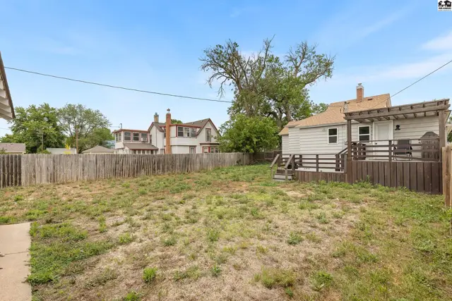 Spacious backyard with a wooden deck, pergola, and privacy fence under a clear blue sky.