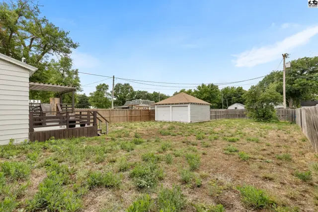 Spacious backyard with a wooden deck, detached two-car garage, and wooden fencing under a clear blue sky.