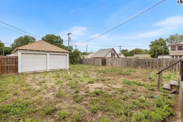 Spacious backyard with a detached two-car garage and wooden fencing under a clear blue sky.