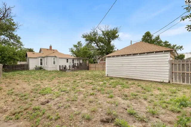 Backyard with a detached garage, wooden fence, and a small house with a deck.