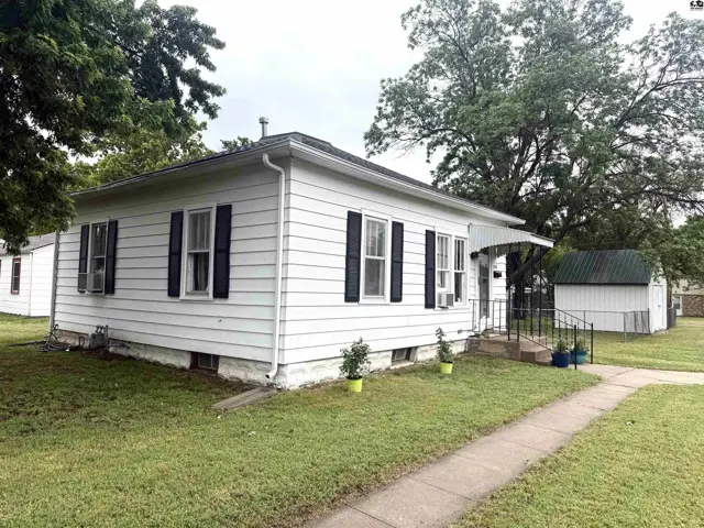 White vinyl-sided house with black shutters, a small porch, and a detached shed.