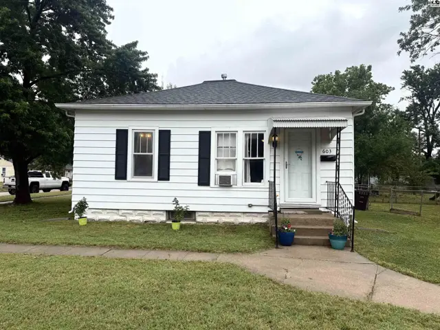 Charming white vinyl-sided bungalow with black shutters and a covered front porch.