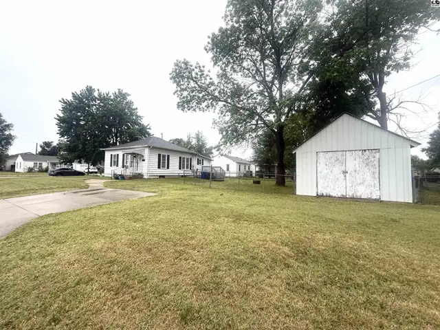 White vinyl-sided house with black shutters and a detached white shed on a grassy lot.