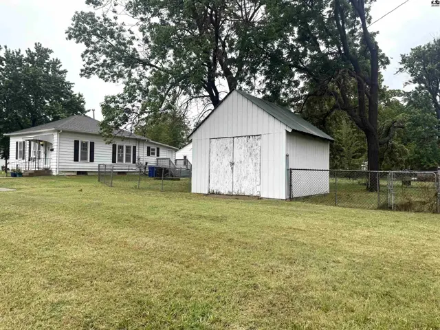 White vinyl-sided house and detached garage with a chain-link fence in a grassy yard.
