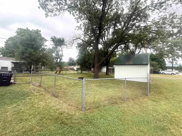 Fenced backyard with a white shed, mature trees, and a playground visible.