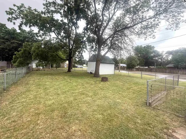 Spacious backyard with mature trees, a white shed, and a chain-link fence.