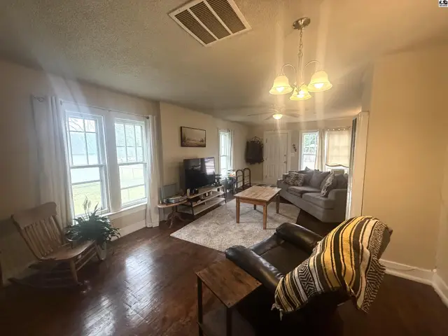 Living room with hardwood floors, large windows, comfortable seating, and a television.