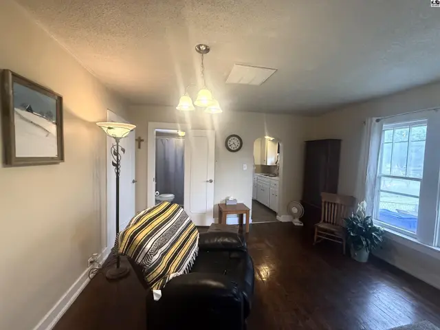Living room with dark wood floors, a recliner, and a view into the kitchen.