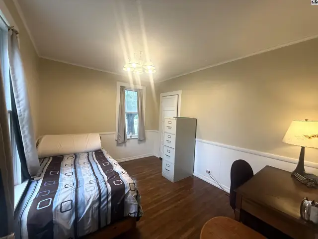 Cozy bedroom with a twin bed, wooden desk, filing cabinet, and hardwood floors.