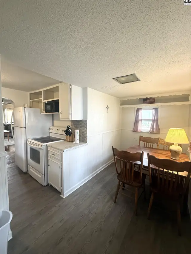 Bright kitchen with white appliances and cabinets adjacent to a dining area with a wooden table and chairs.