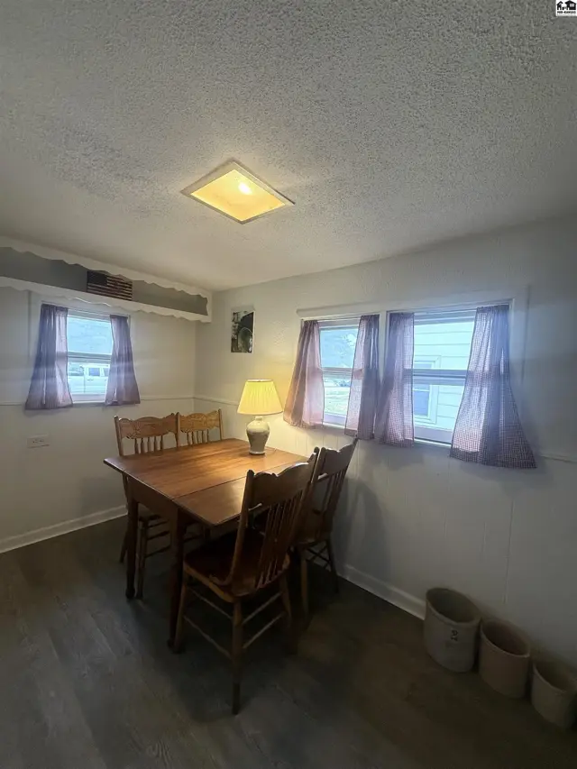 Dining area with wooden table and chairs, light wood flooring, and purple sheer curtains.