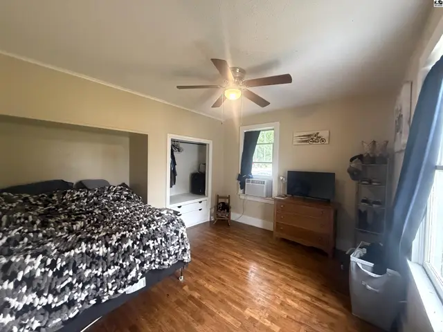 Spacious bedroom with hardwood floors, ceiling fan, built-in closet, and a dresser with a television.