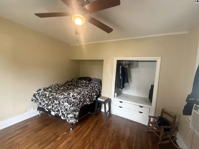 Bedroom with hardwood floors, a ceiling fan, and a built-in closet with hanging clothes.