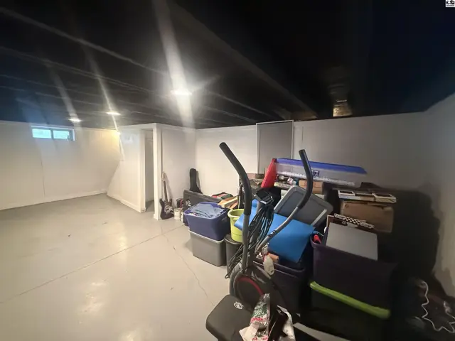 Unfinished basement with white walls, concrete floor, and storage items.