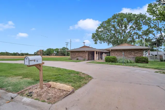 Brick ranch home with a circular driveway, mailbox, and mature trees under a blue sky.
