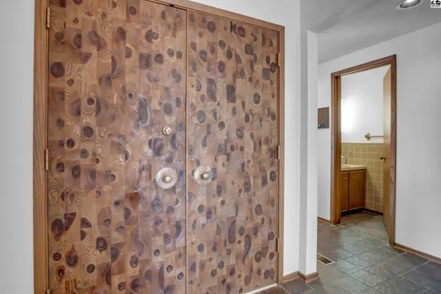 Unique wood-paneled double doors with brass hardware open to a hallway with a glimpse of a bathroom.