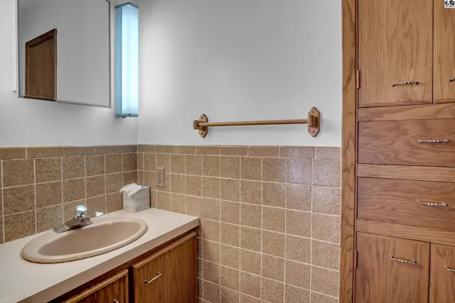Bathroom vanity with beige tile, wood cabinets, and a tall linen closet.