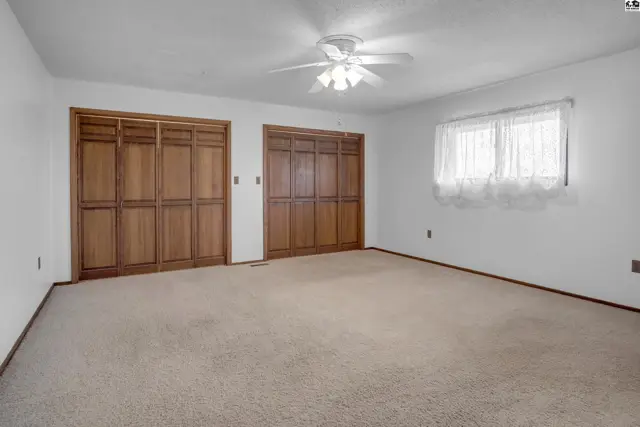 Spacious bedroom with plush carpet, white walls, and two large wooden closet doors.
