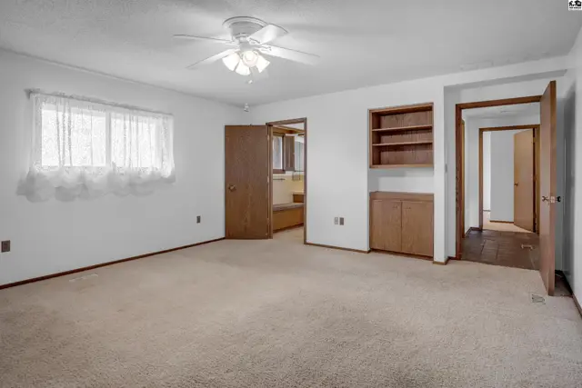 Spacious bedroom with plush carpet, built-in shelving, and a ceiling fan.
