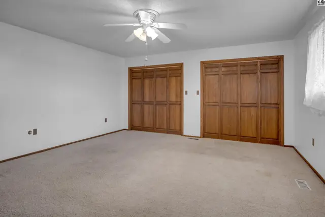 Spacious bedroom with plush carpet, white walls, and two large wooden closet doors.