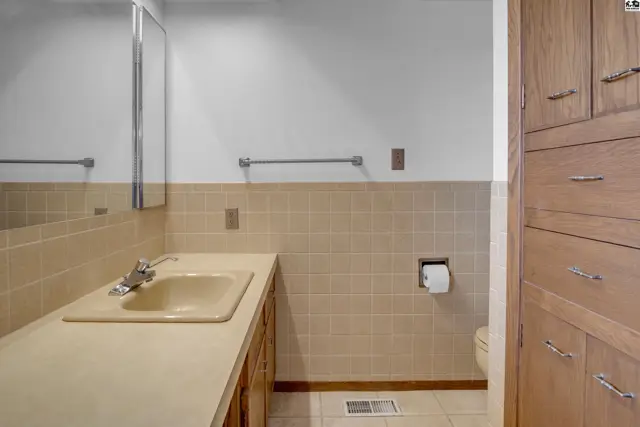 Spacious bathroom with a beige vanity, tiled walls, and ample wood cabinetry.