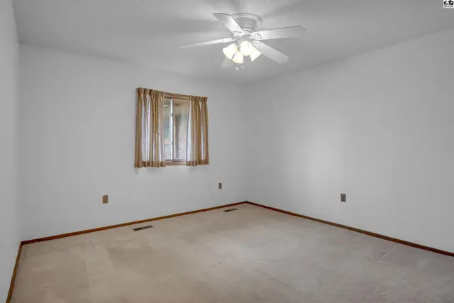 Spacious bedroom with neutral carpet, white walls, and a ceiling fan.
