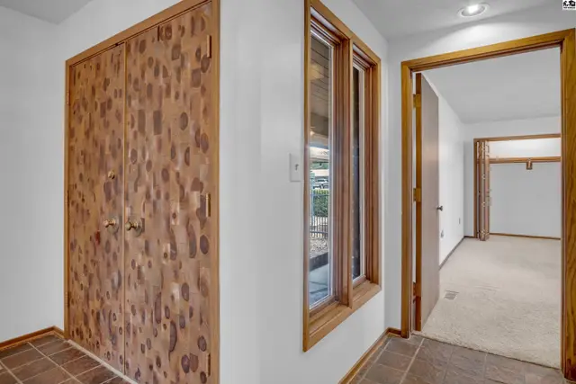 Hallway with large knotty wood closet doors, tile floor, and view into a carpeted room.