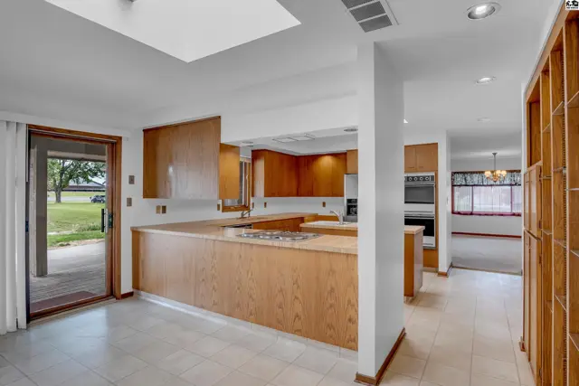Spacious kitchen with light wood cabinetry, a gas stovetop island, and tiled flooring.
