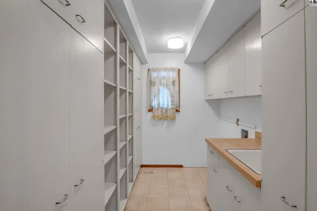 Spacious laundry room with ample white cabinetry, extensive shelving, and a light wood countertop with sink.