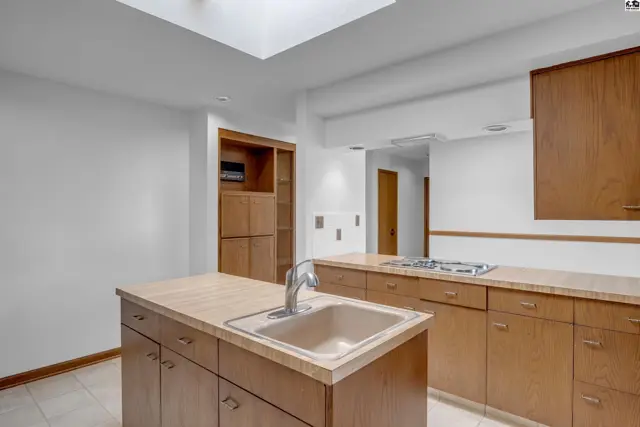 Spacious kitchen features a large island with sink, wood cabinetry, and a gas stovetop.