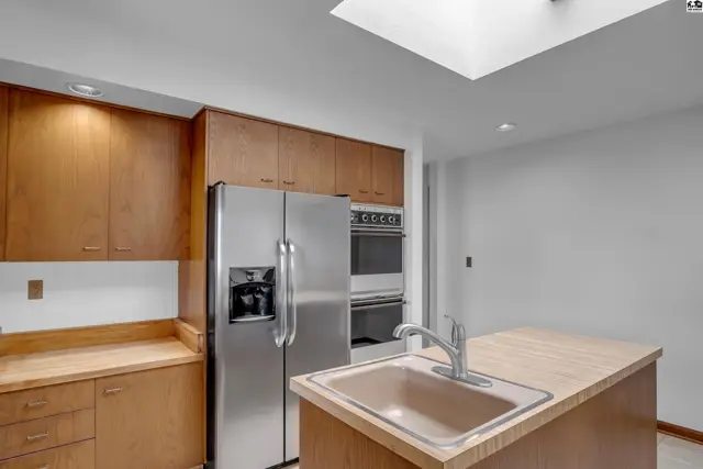 Modern kitchen with stainless steel appliances, wood cabinetry, and a central island with a sink.