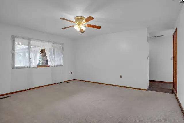 Spacious living room with neutral carpet, white walls, and a wood-trimmed ceiling fan.