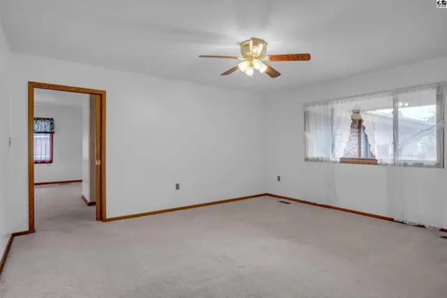 Spacious living room with neutral carpet, white walls, wood trim, and a ceiling fan.