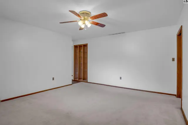 Spacious room with neutral carpet, white walls, wood trim, and a ceiling fan.