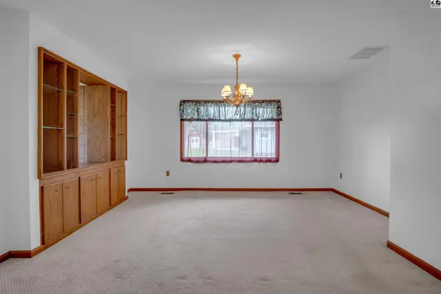 Spacious dining room with built-in oak cabinetry, neutral carpet, and a decorative chandelier.