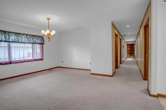 Spacious living room with plush carpet, large window, and a hallway leading to bedrooms.