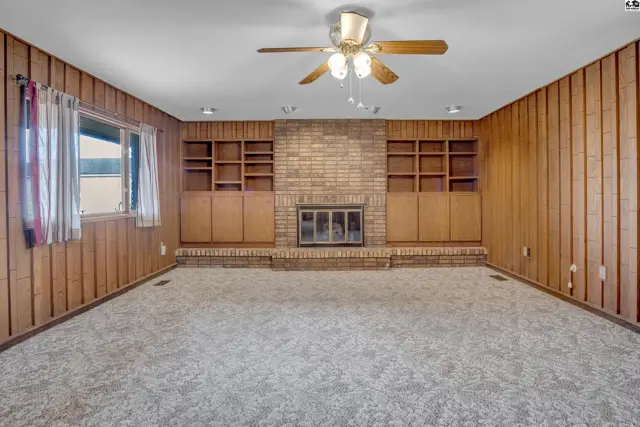 Spacious living room features a brick fireplace, built-in shelving, wood paneling, and plush carpet.