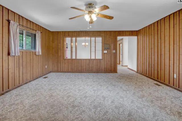 Spacious living room with wood-paneled walls, plush carpet, and a decorative glass partition.