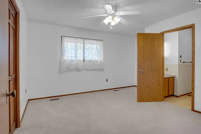 Spacious bedroom with plush carpet, white walls, and a ceiling fan, opening to an ensuite bathroom.
