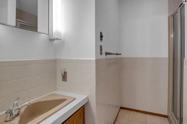 Bathroom with beige sink, white tiled walls, and a glass-enclosed shower stall.