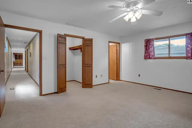 Spacious bedroom with plush carpet, bi-fold closet doors, and a ceiling fan.