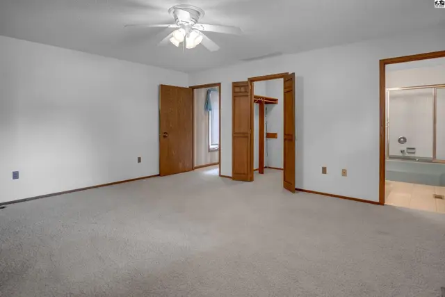 Spacious bedroom with plush carpet, white walls, wood doors, and an ensuite bathroom with a tub.