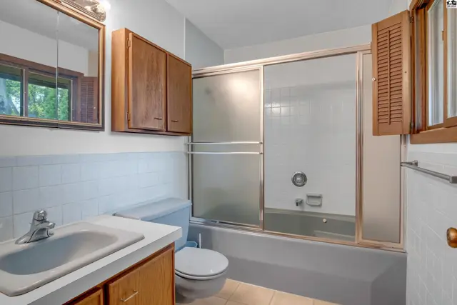A bathroom with a light blue toilet, white tiled walls, and a wooden vanity and medicine cabinet.