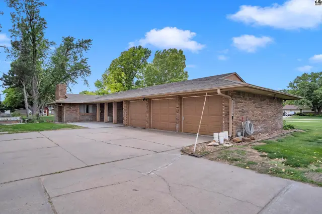 Spacious brick home with a four-car garage and mature trees under a blue sky.