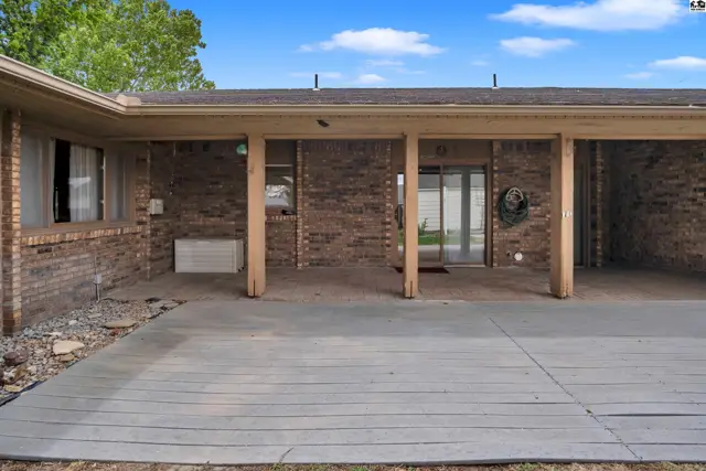 Covered patio with brick exterior and concrete flooring, featuring wooden support columns.