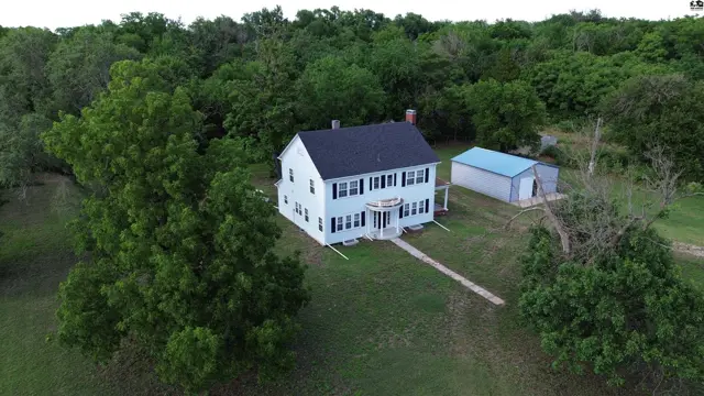 Light blue farmhouse with black shutters and a detached metal garage sits on a grassy lot.