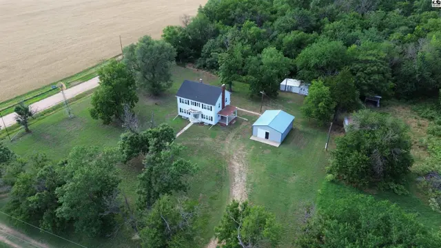 White farmhouse with a red-brick porch, surrounded by mature trees and outbuildings.