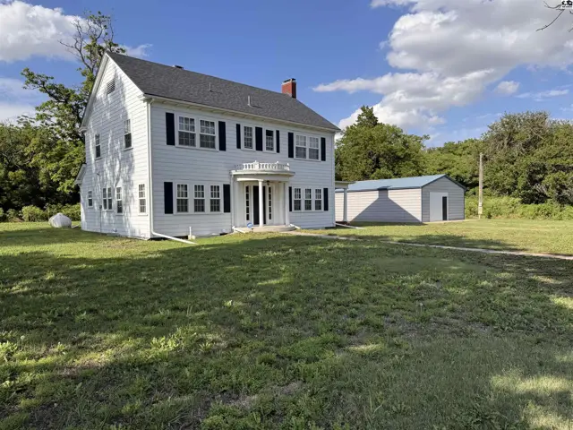 Classic white two-story home with black shutters and a detached garage sits on a grassy lot.